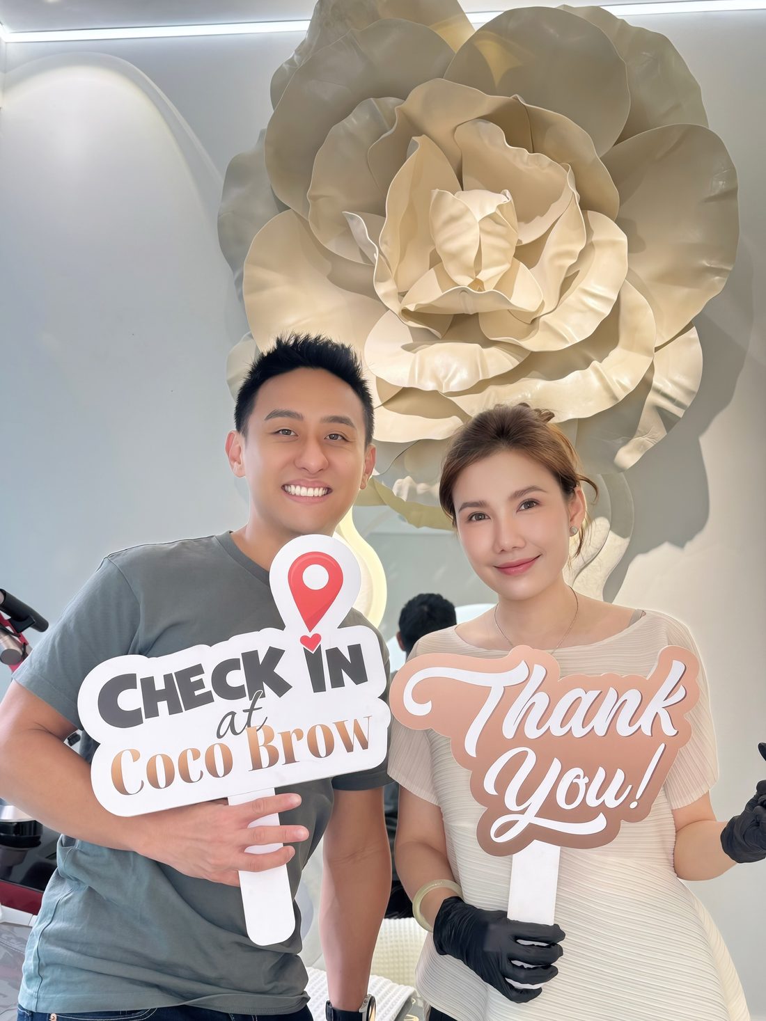 Male client holding a Check in at Coco Brow board next to Master Coco Le